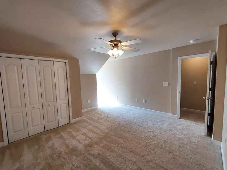 Long bonus room with a sloped ceiling, warm beige walls and white bifold closet doors