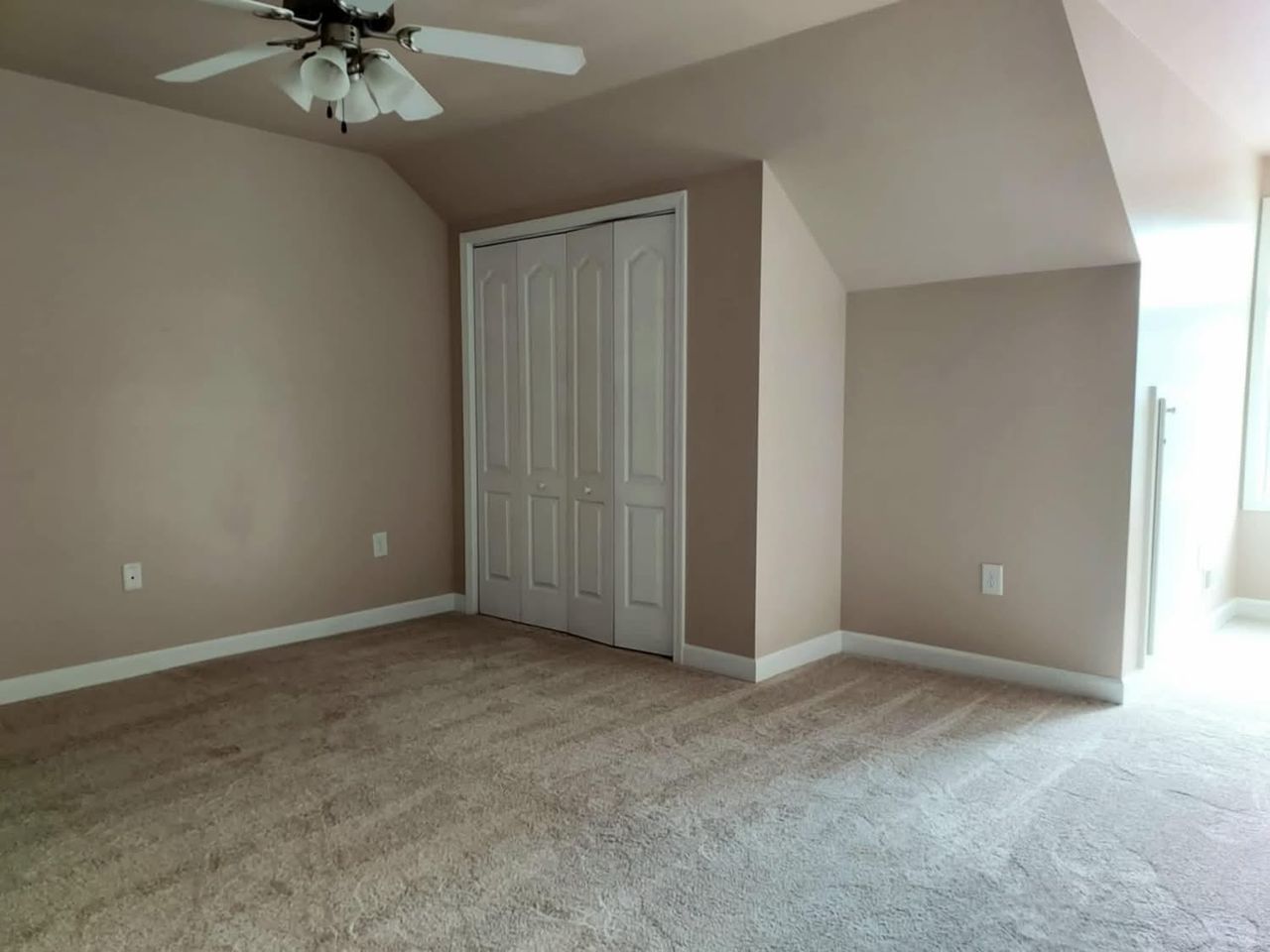 Bedroom with an angled ceiling, beige walls and white closet doors