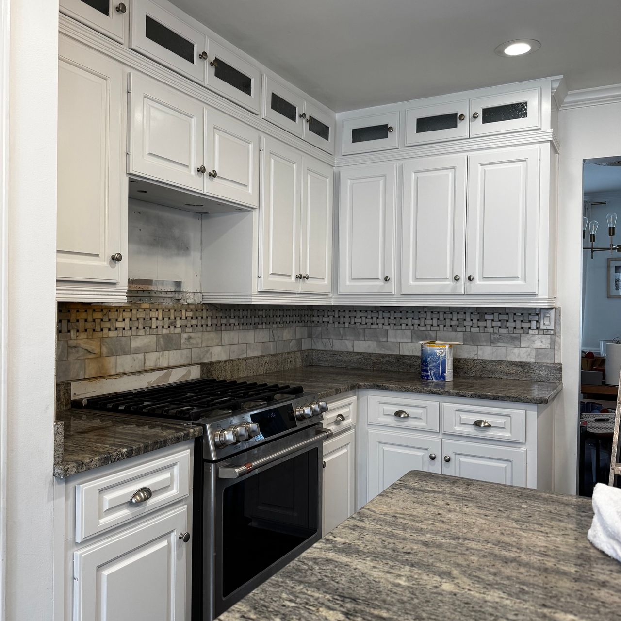Kitchen cabinets painted white with glass-front uppers, a tile backsplash and dark granite counters