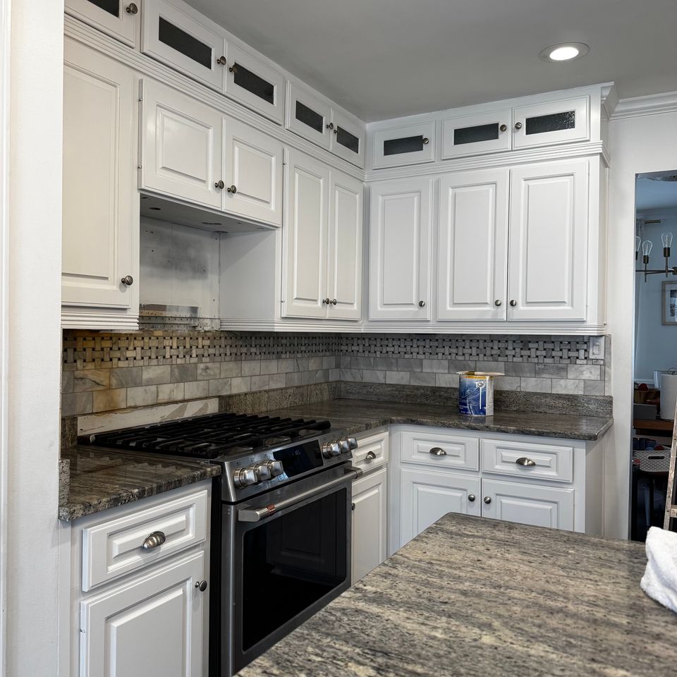 Kitchen cabinets painted white with glass-front uppers, a tile backsplash and dark granite counters