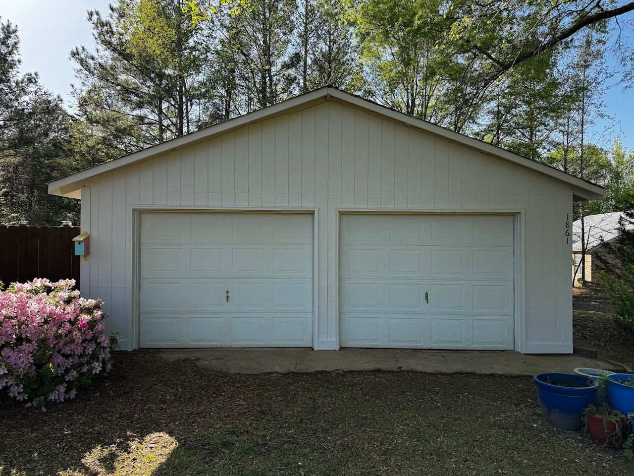 Detached two-bay garage with board and batten siding freshly painted cream and white garage doors