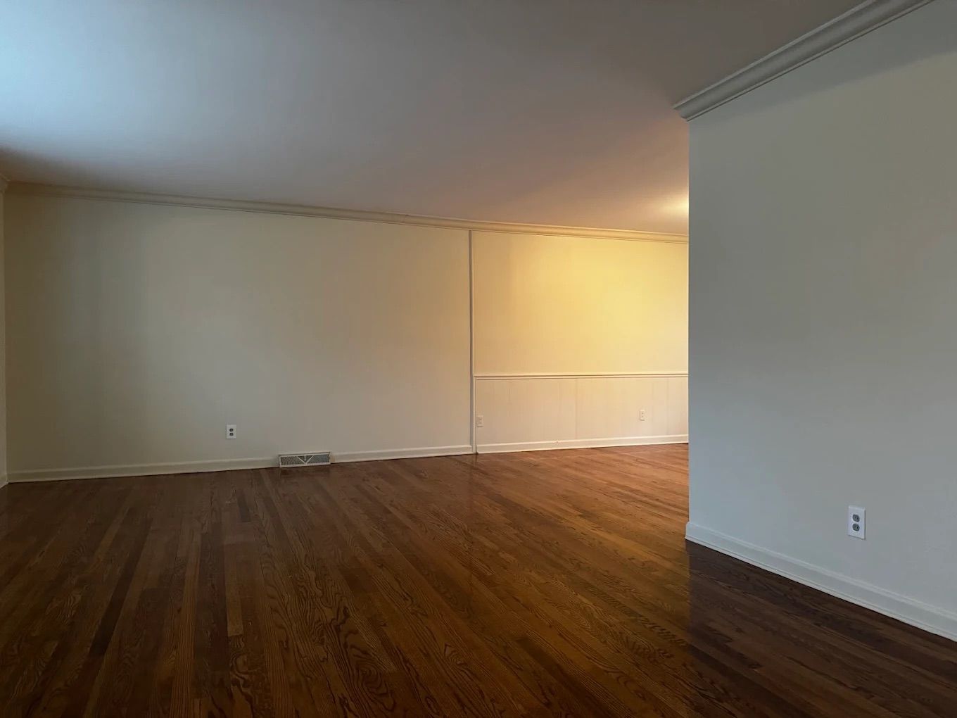 Long open room with freshly painted white walls, ceiling and crown molding over wood floors